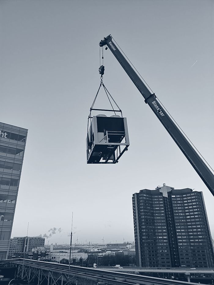 Een koelmachine hangt aan de kraan boven de Rotterdamse skyline
